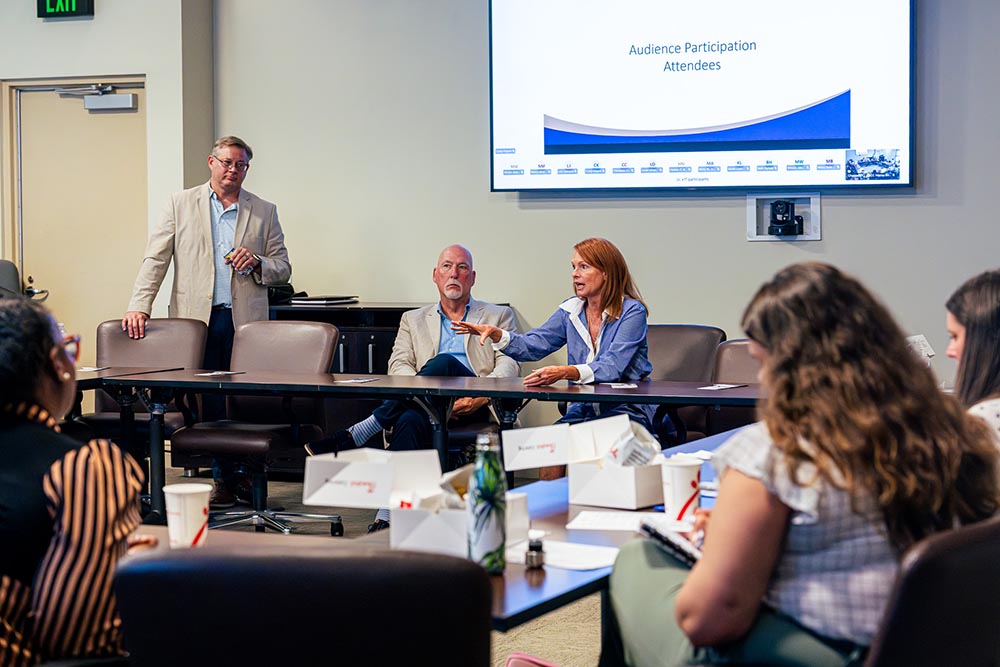 A panelist gestures toward the audience while presenting the audience participation slide.