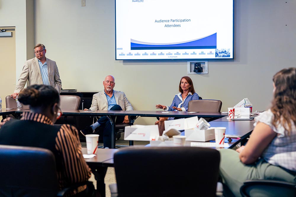 Wide view of the meeting room with the presentation on screen and attendees at the table.